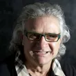 A man wearing glasses and a plaid shirt smiles for the camera